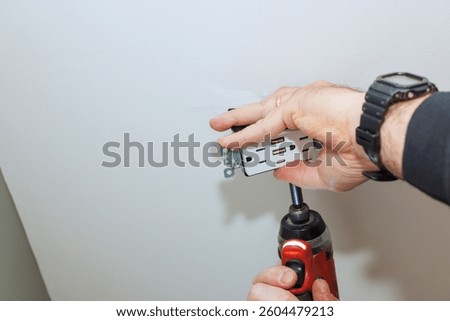 Worker hands secure an electrical outlet to ceiling using cordless drill in home improvement activity.