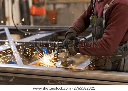 Worker hands and torso operating angle grinder on metal construction with shower of sparks in workshop