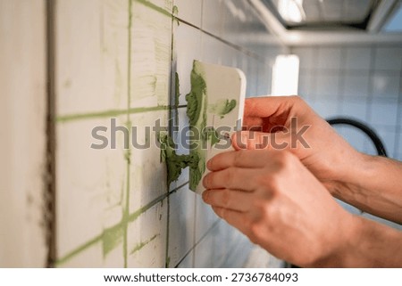Worker hands using a spatula to apply green grout into ceramic bathroom wall tile joints, creating a smooth, clean finish during a kitchen, bathroom renovation diy project