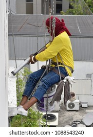 A worker hanging from the top of building inject silicone rubber to repair building's cracks before repainting color process