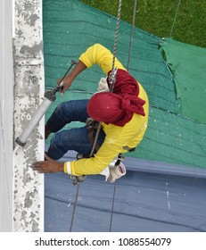 A worker hanging from the top of building inject silicone rubber to repair building's cracks before repainting color process