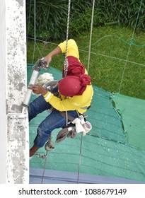 A worker hanging from the top of building inject silicone rubber to repair building's cracks before repainting color process