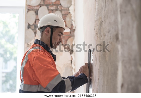 A worker in a helmet makes repairs in the
apartment,finishing work. A man is engaged in interior decoration
of the building, wall putty