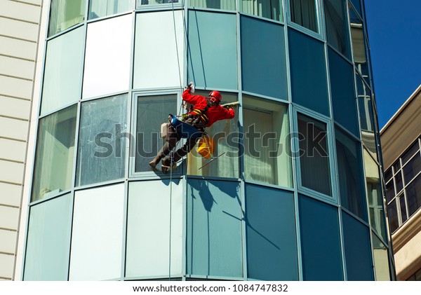 worker in a helmet washes the\
window of a high-rise building from the outside, hanging on a\
rope