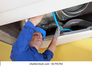 Worker holding blue pipe in place under air ducts
