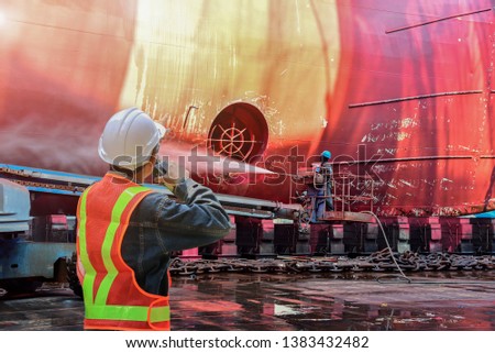 worker holding communication radio, Supervisor for workers ship washing or cleaning by jet water high pressure at floating dry dock in shipyard.