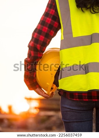 Worker holding helmet and uniform on construction site, engineer against sunset
