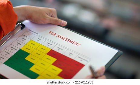 A Worker Is Holding Risk Assessment Paper Form, Preparing To Do Project Evaluation, With Blurred Background Of Factory Place. Industrial Working Scene Action Photo. Selective Focus.