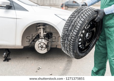 Worker holding spare wheel near broken car