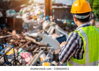 A worker holding a tablet looks at a pile of steel for recycling at a recycling plant. Recycle waste. - Powered by Shutterstock