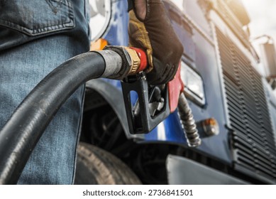 A worker holds a fuel nozzle while filling a truck with gasoline at a station.