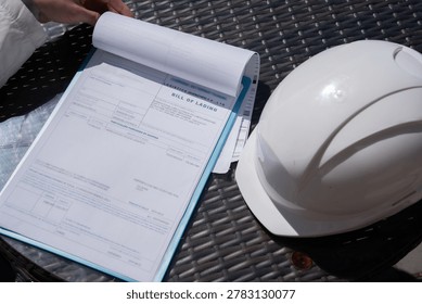 The worker holds a tablet with documents or bill of lading a protective helmet.