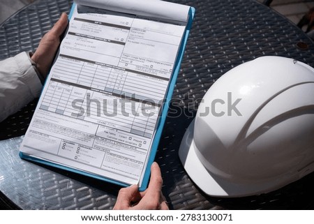 The worker holds a tablet with documents or bill of lading a protective helmet