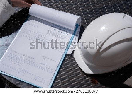 The worker holds a tablet with documents or bill of lading a protective helmet.