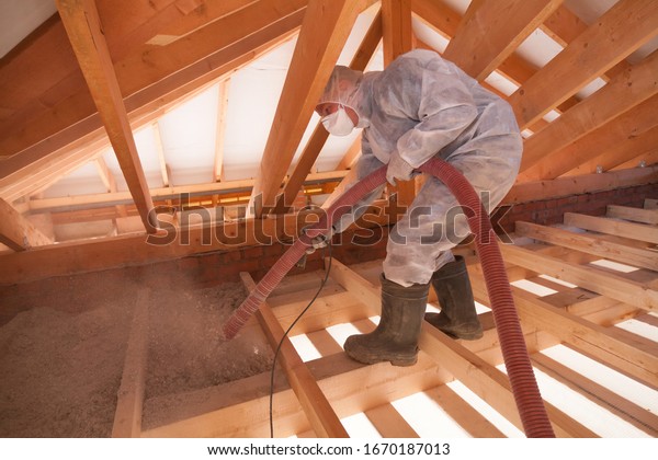 Worker with\
a hose is spraying ecowool insulation in the attic of a house.\
Insulation of the attic or floor in the\
house