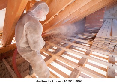 Worker with a hose is strewing ecowool insulation in the attic of a house. Insulation of the attic or floor in the house