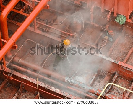 Worker hydro blasting on main deck of ship at shipyard.