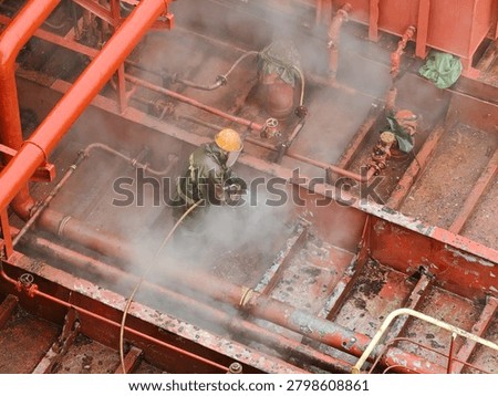 Worker hydro blasting on main deck of ship at shipyard.