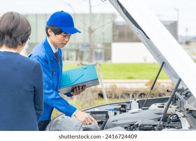A worker inspects a car with the driver.  Road service.