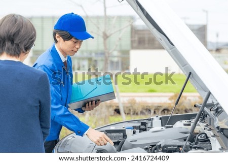 A worker inspects a car with the driver.  Road service.