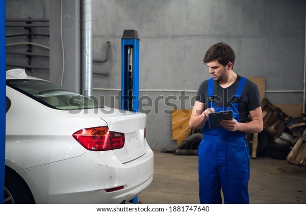 Worker inspects a car\
and uses a tablet