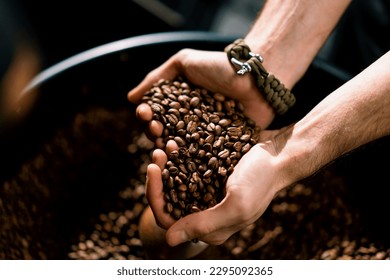 A worker inspects fragrant roasted coffee beans taking them in his hands at production plant close-up - Powered by Shutterstock