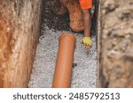 Worker Installing Drainage Pipe In Trench During Construction