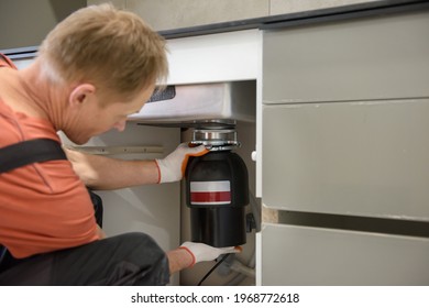 The Worker Is Installing A Household Waste Shredder For The Kitchen Sink.