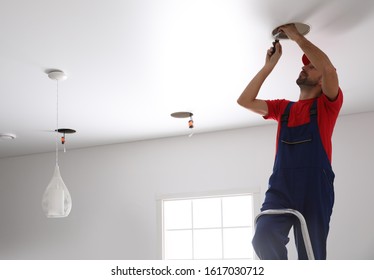 Worker installing lamp on stretch ceiling indoors. Space for text