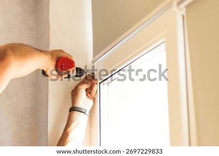 Worker installing mechanisms and brackets for roller blinds on window frame.