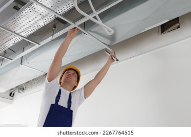 Worker installing metal frame indoors. Suspended ceiling