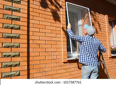 Worker installing mosquito net or mosquito wire screen on brick house window.