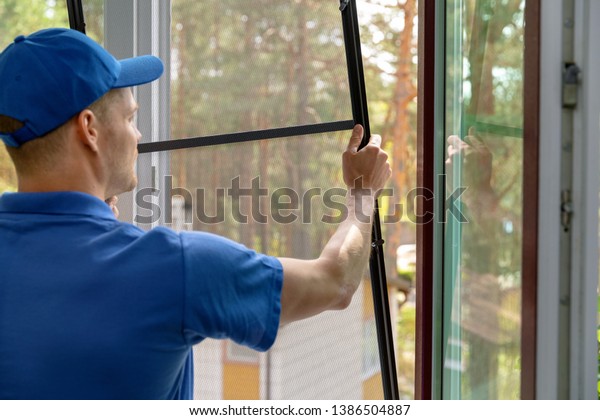 worker installing mosquito net wire mesh in plastic\
window frame