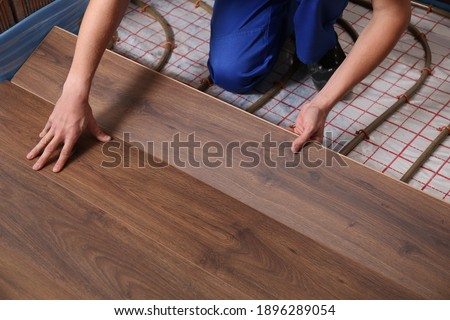 Worker installing new wooden laminate over underfloor heating system, closeup
