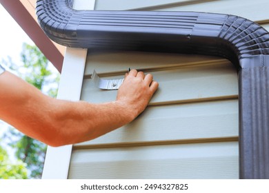 An worker is installing rain gutter on roof is fitting downpipe bending downspout