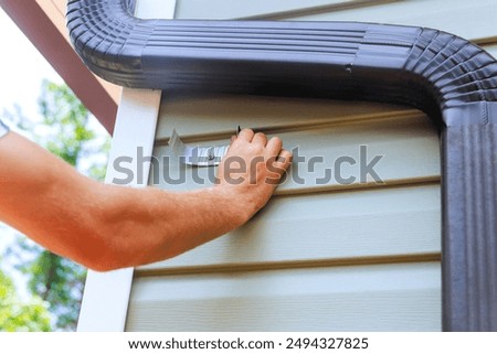 An worker is installing rain gutter on roof is fitting downpipe bending downspout