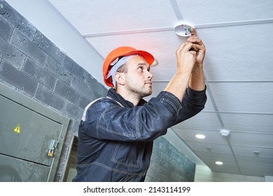 worker installing smoke detector on the ceiling. Fire alarm system installation