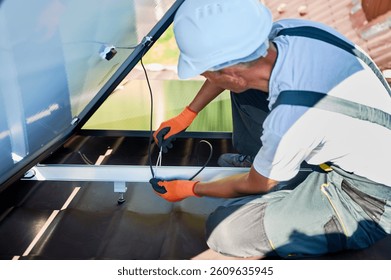 Worker installing solar panels system on rooftop of house. Close up view of electrician securing cables by special tie. Concept of alternative and renewable energy.
