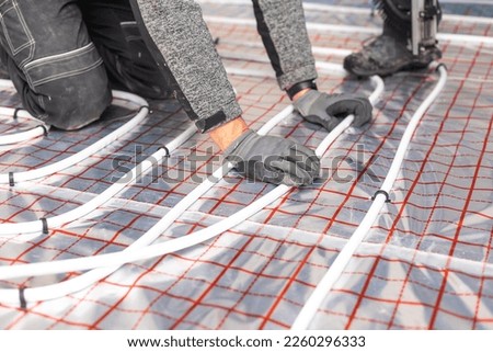 Worker installing underfloor heating system, water heating on the new residential house, concept of heated floor