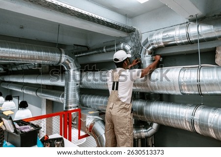 Worker installing ventilation ductwork in industrial setting during daytime at a construction site