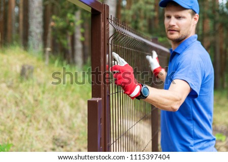 worker installing welded metal mesh fence