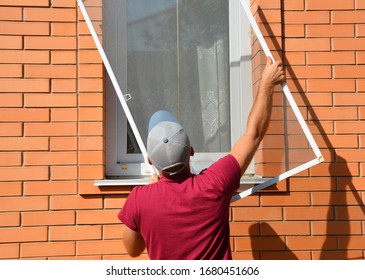 A worker is installing a window mosquito net, fly screen or insects screen to protect the house from insects in summer.
