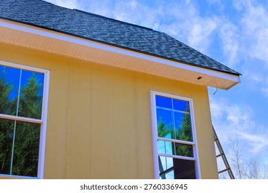 Worker installing yellow primed smooth siding house with tall windows, ladder in place
