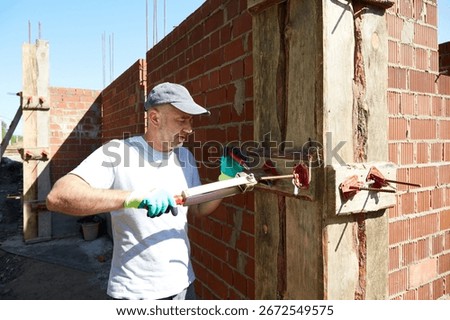 A worker installs a spring clamp for securing the formwork on the construction site. Work on the construction of the house, preparation for pouring the foundation.