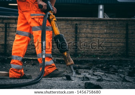 worker jack hammering out broken sections of asphalt wearing hi vis trousers 