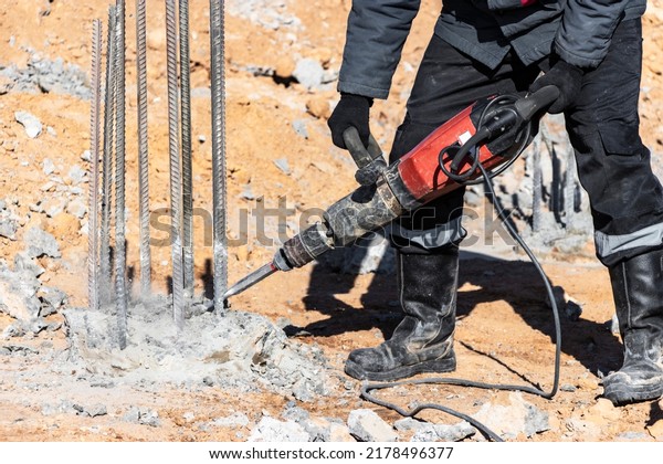 A worker with a jackhammer breaks concrete\
piles. Felling the pile head with a hand tool. Preparation of piles\
for mounting the foundation