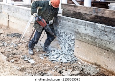 A worker with a jackhammer at a construction site levels a concrete wall. Powerful manual industrial equipment. Difficult construction job. Selective focus