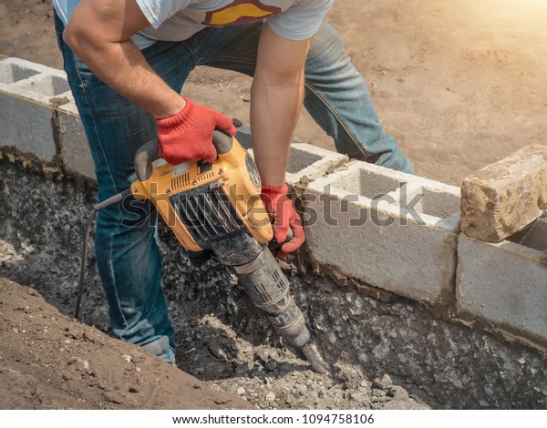 Worker\
with a jackhammer, foundation, building\
blocks