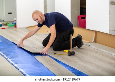 Worker joining click lock vinyl floor plank covering at home renovation. Man laying PVC-floor. Craftsman installing new laminated wooden floor on blue acoustic thermal flooring underlayment. - Shutterstock ID 1912419679