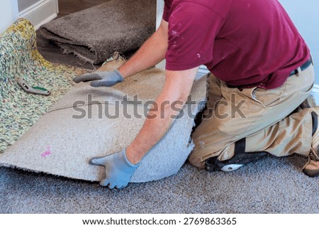 Worker kneels, pulls up an old carpet to prepare floor for new installation in house.